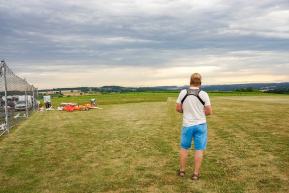 Mann steht auf Flugplatz und fliegt mit seinem Modell